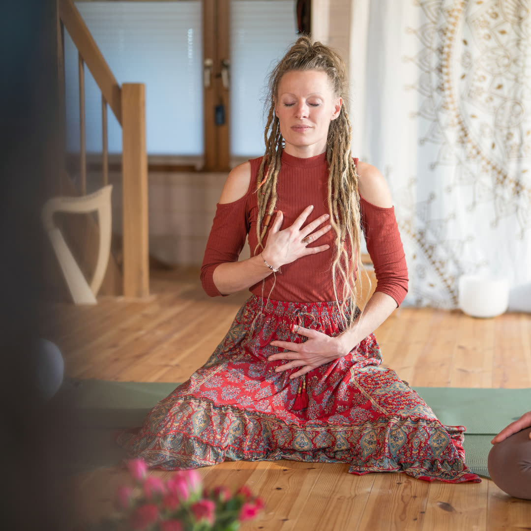 Lydia sitzt mit geschlossenen Augen im Yogaraum, eine Hand auf dem Herzen